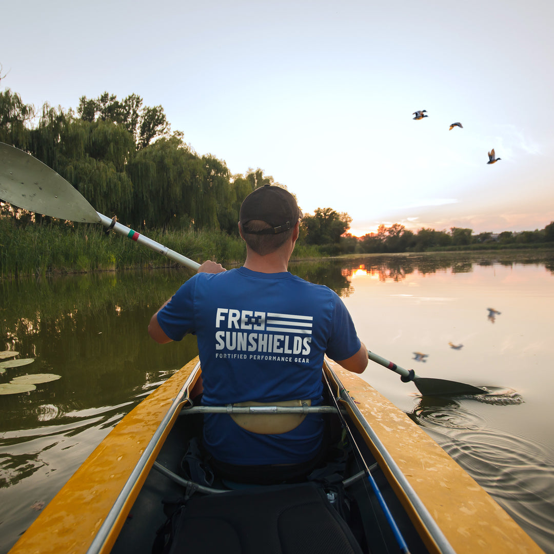 lifestyle image of a man's back in a yellow kayak. He's wearing a blue short sleeve upf shirt with a white Free Sunshields logo on the back. 