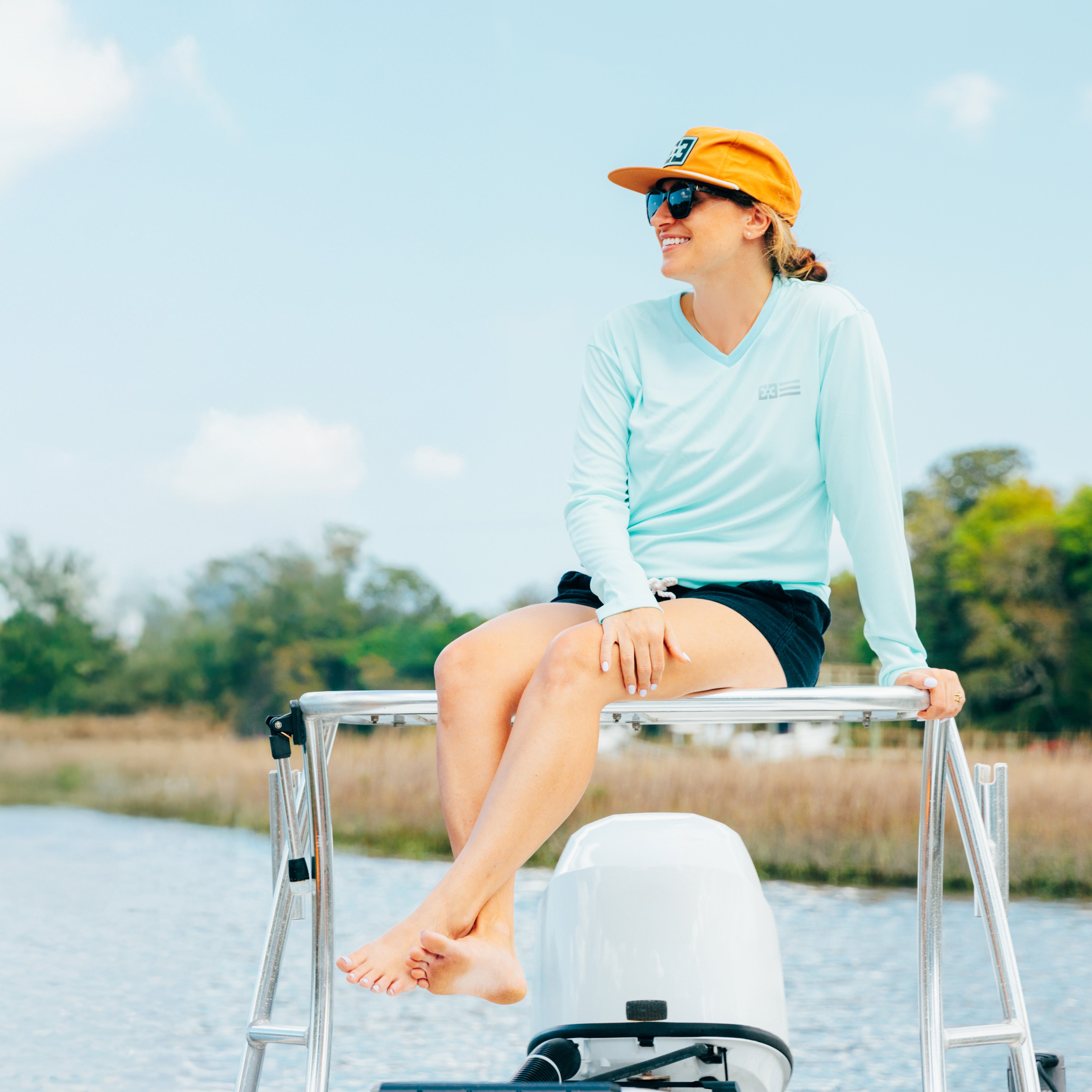 lifestyle image of a woman wearing a women's long sleeve upf shirt. She sits on the roof of a fishing boat wearing an original free sunshields rope hat. 