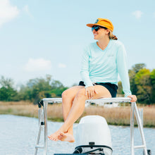 lifestyle image of a woman wearing a women's long sleeve upf shirt. She sits on the roof of a fishing boat wearing an original free sunshields rope hat. 