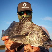 man holding largest caught fish wearing sunglasses free sunshields hat and 3d camo neck gaiter mask
