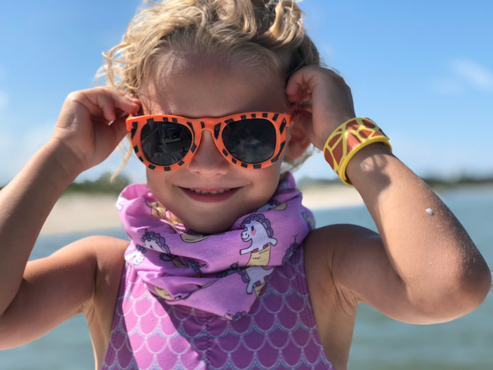 Smiling Child on ocean wearing free sunshields sunglasses and unicorn mermaid neck gaiter headband