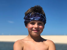 youth boy smiling on blue ocean beach wearing shark bait neck gaiter headband