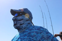 man wearing blue scales neck gaiter mask on ocean boat with fishing poles